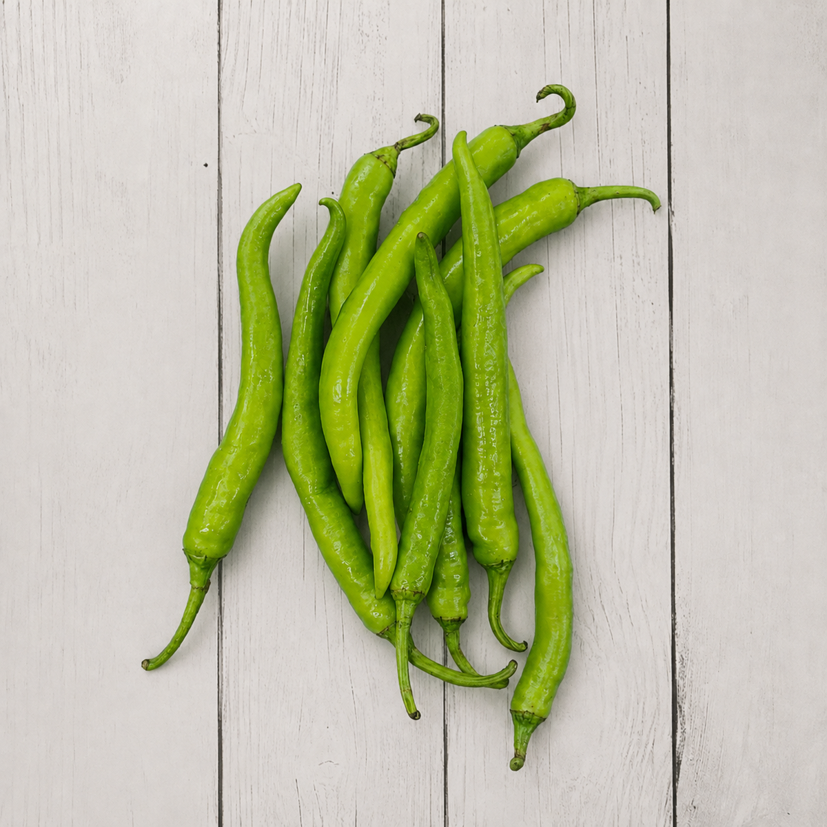 A pile of fresh, bright green chili peppers arranged on a light gray wooden plank surface.