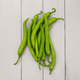 A pile of fresh, bright green chili peppers arranged on a light gray wooden plank surface.