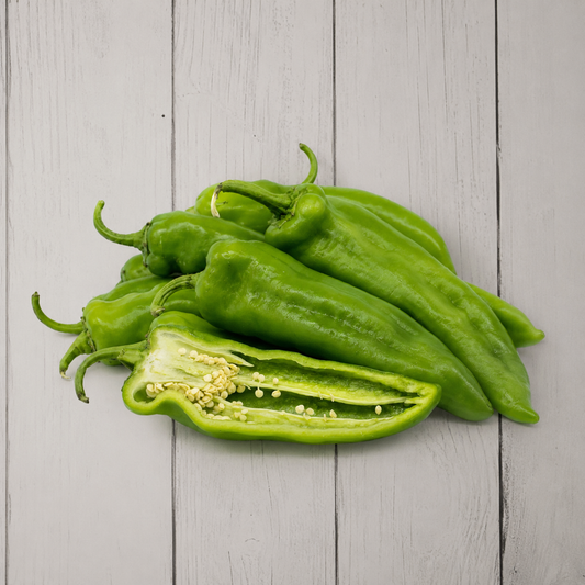 A pile of fresh green bell peppers on a light gray wooden plank surface, with one pepper cut open to show the inside seeds and flesh.