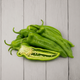 A pile of fresh green bell peppers on a light gray wooden plank surface, with one pepper cut open to show the inside seeds and flesh.