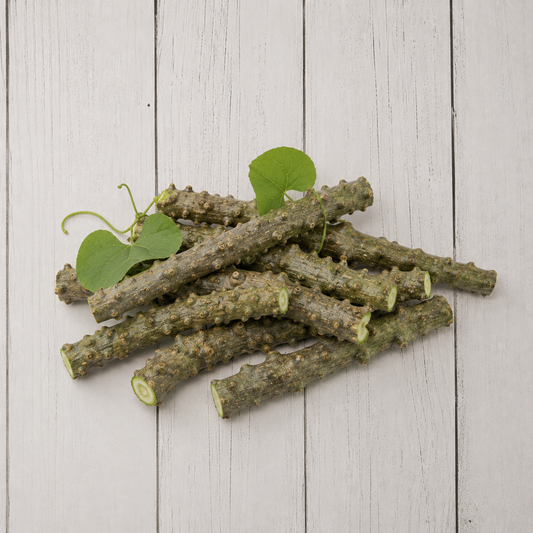 A pile of natural green vine stems with small leaves, arranged on a light gray wooden plank surface.
