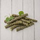 A pile of natural green vine stems with small leaves, arranged on a light gray wooden plank surface.
