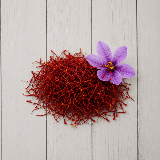 A pile of bright red saffron threads with a single purple saffron flower on a light gray wooden plank background.