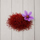 A pile of bright red saffron threads with a single purple saffron flower on a light gray wooden plank background.