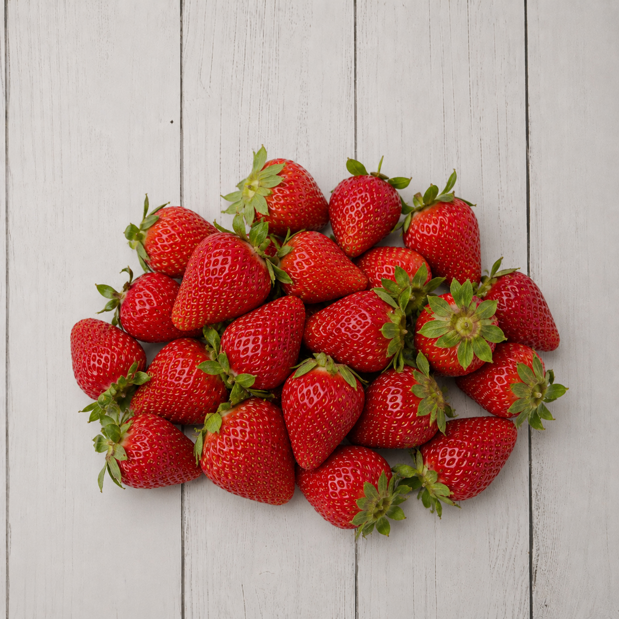 A pile of fresh red strawberries with green tops arranged on a light gray wooden plank surface.