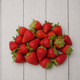 A pile of fresh red strawberries with green tops arranged on a light gray wooden plank surface.
