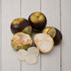 Several coconuts on a light gray wood plank background, with two coconuts whole and two halves showing the white flesh inside, plus four translucent white pearls in front.